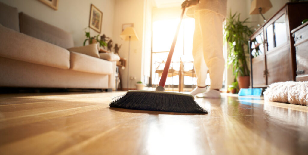 Unrecognizable woman sweeping the parquet floor, window light reflection.